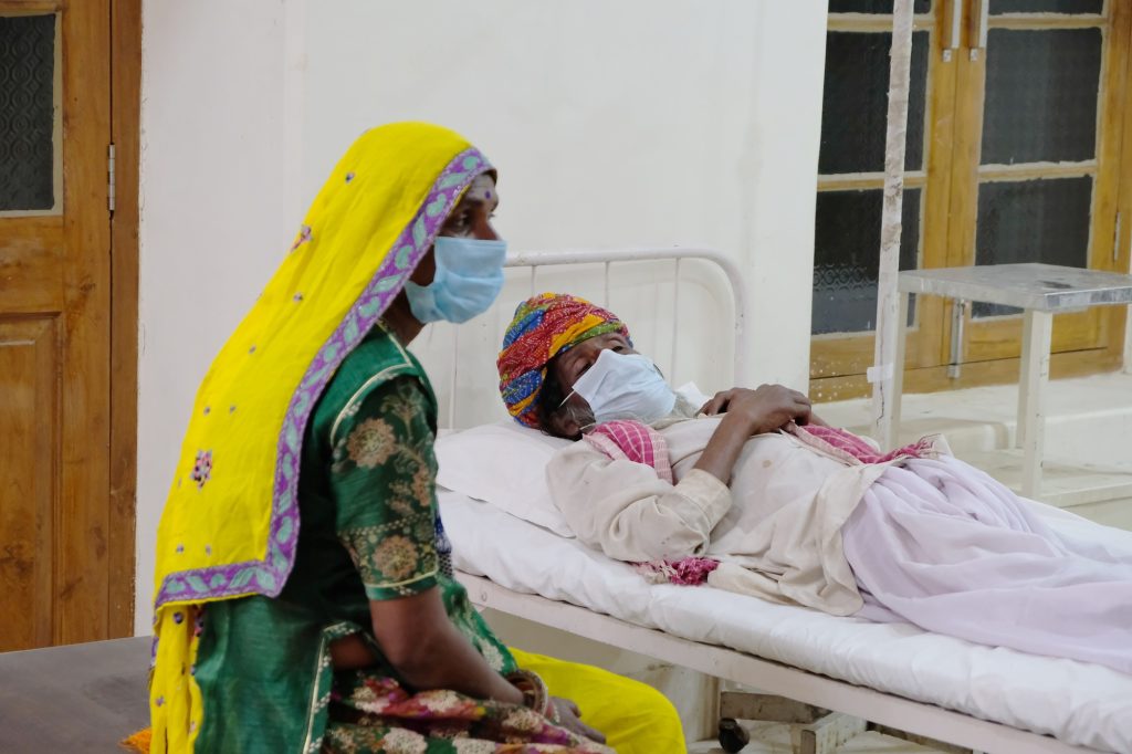 Elderly Indian female in a medical mask sitting near her husband in a hospital